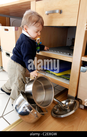 Kleiner Junge, Baby, 10 Monate alt, ist die Erkundung der Küche, spielt mit Kochtöpfen. entfernt die Töpfe aus Küchenschrank. Stockfoto