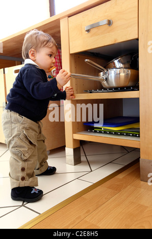 Kleiner Junge, Baby, 10 Monate alt, ist die Erkundung der Küche, spielt mit Kochtöpfen. entfernt die Töpfe aus Küchenschrank. Stockfoto