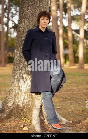 Eine schöne junge Frau lehnt sich an einen Baum im Winter. Stockfoto