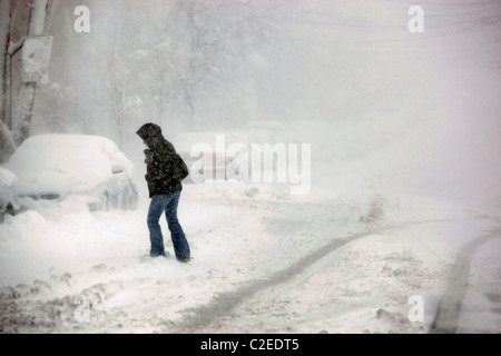 Eine Frau kreuzt eine schneebedeckte Straße bei einem Wintersturm in Boston, Massachusetts Stockfoto