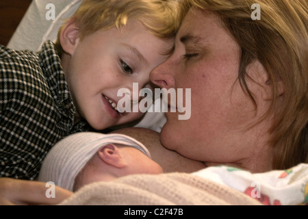 Ein vier Jahre alter Junge, der seinen Neugeborenen Bruder, als seine Mutter kennenlernen blickt auf. Stockfoto