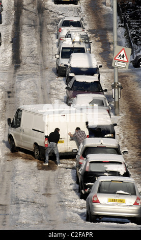 Zwei Männer schieben einen van auf einer steilen Straße in Glasgow, Schottland, der in Eis und Schnee machen fahren und zu Fuß schwer fällt. Stockfoto