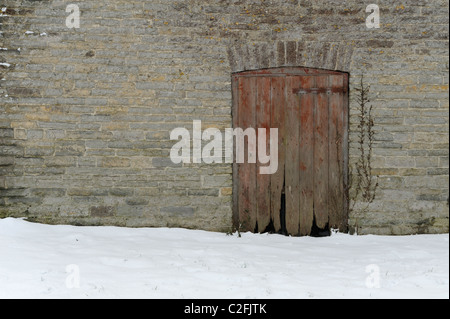 Eine alte rote Scheune Holztür, ein landwirtschaftliches Gebäude im Winter mit Schnee auf dem Boden entnommen. Stockfoto