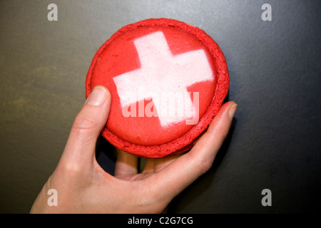 Frau Hand mit einer Mandel-Makronen-Makronen-Kuchen / Torten mit Schweizerkreuz verziert. Genf / Genève Schweiz. Stockfoto