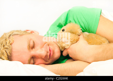 Closeup Portrait eines jungen Mannes schläft auf dem Bett umarmt seine weiche Hundespielzeug Stockfoto