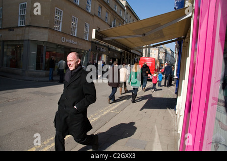 Ein Mann in einen Mantel eilt durch eine Einkaufsstraße. Stockfoto