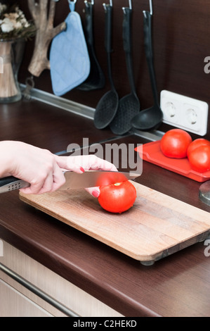 Schöne glücklich lächelnde Frau in Küche Interieur schneidet eine Tomate auf ein Schneidebrett. Nur eine person Stockfoto