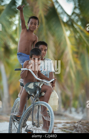 Drei Heimatinsel jungen auf einem Fahrrad unten Insel Coral, Palme gesäumten Straße. Stockfoto