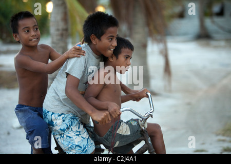 Drei Heimatinsel jungen auf einem Fahrrad unten Insel Coral, Palme gesäumten Straße. Stockfoto