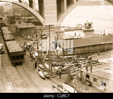 Kanus im Überfluss wie Hochwasser am Ufer unter Betonbrücke und neben Eisenbahnwaggons Trichter Runde. Stockfoto