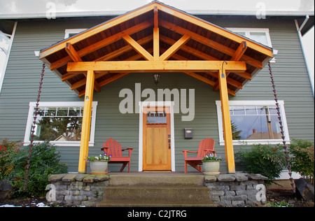 Mission-Stil gebeizt Holz Haustür mit abgeschrägten Glas umgeben von zwei Adirondack Stühle und Blumen Stockfoto