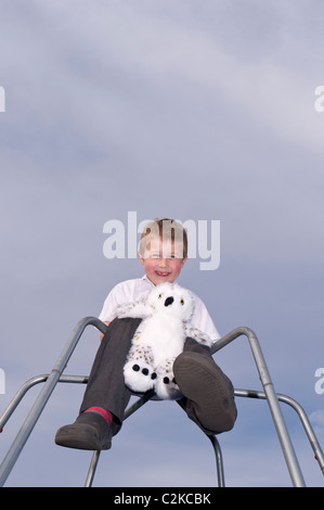 Ein MODEL Release Bild ein sieben Jahre alter Junge und sein Kuscheltier im Freien auf einem Klettergerüst im Vereinigten Königreich Stockfoto
