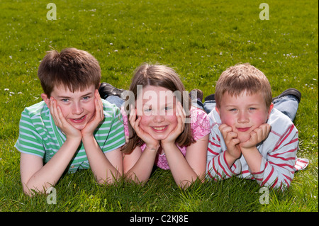 Ein MODEL Release Bild von einem Mädchen und zwei jungen (7, 9 und 11) Verlegung im Freien auf dem Rasen im Vereinigten Königreich Stockfoto