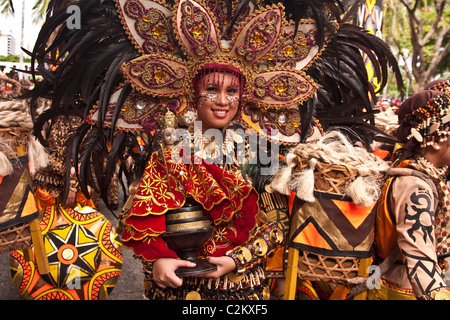 Eine Stammes-Dame in Perlen Kostüm und gefiederten Kopfschmuck hält ein Sto. Nino-Figur. Stockfoto