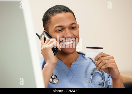 Afrikanische amerikanische Arzt am Telefon sitzen am Computer betrachten seiner Kreditkarte Stockfoto