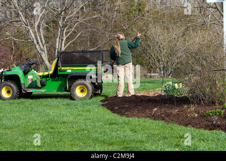 Verbreitung von Mulch im Garten mit einem John Deere Gator TX und einer Mistgabel. Stockfoto