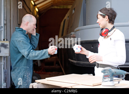 Mann und Frau eine Pause von Arbeiten für den Bau eines Bootes, eine Tasse Tee trinken und am Telefon zu sprechen. Stockfoto