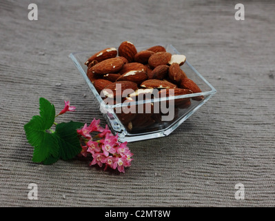 Mandeln in einer Glasschale quadratisch auf der Serviette mit Blume Stockfoto