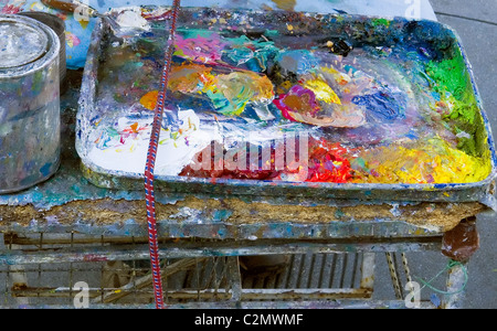 Eine lebendige, hochauflösende Nahaufnahme eines unordentlichen, gut gebrauchten Metallkünstlers, der mit einer chaotischen Mischung aus farbenfrohen Öl- oder Acrylfarben überflutet wird Stockfoto