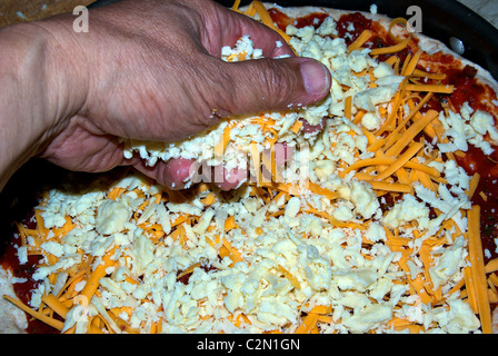 Prise geriebener Cheddar Mozarella Käse reichen Tomatensauce auf Pizza-Brot-Teig in Pfanne Stockfoto