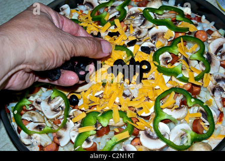 Platzieren in Scheiben geschnittenen schwarzen Oliven grüne Paprika Pilze Scheiben über geriebenen Käse gewürfelt Zwiebel tiefen Pfanne Peperoni-pizza Stockfoto