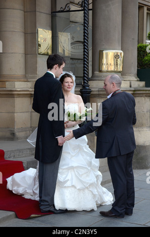 Hochzeitsfotograf stellt die Braut und Bräutigam vor dem Balmoral Hotel an der Princes Street, Edinburgh. Stockfoto