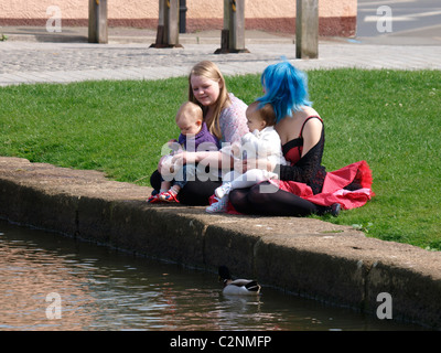 Zwei junge Mütter und Säuglinge saß am Wasser füttern Enten, Bude, Cornwall, UK Stockfoto