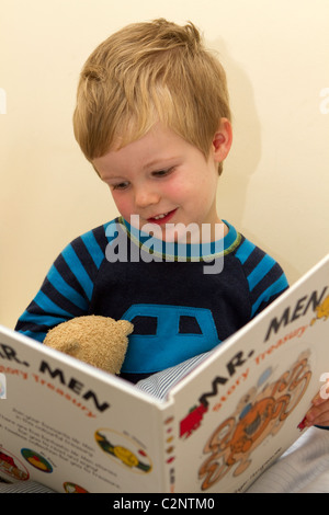 Kleiner Junge liest ein Buch auf seinem Bett. Stockfoto
