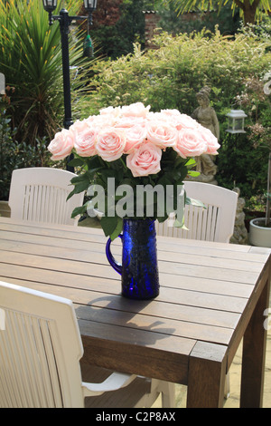 Eine schöne Vase mit Rosen auf einem Terrassentisch an einem sonnigen Tag Stockfoto