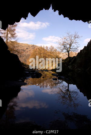 Silhouette des Rydal Höhleneingang mit Reflexion der sonnenbeschienenen Lakeland Fells gegenüber, Rydal, Lake District, Cumbria, UK Stockfoto