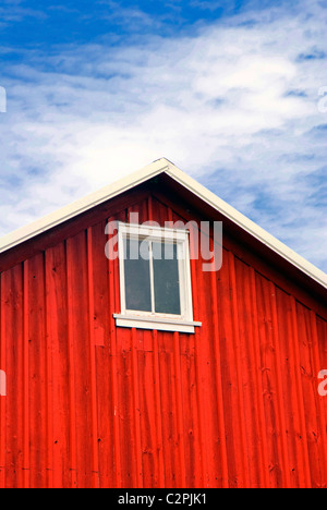 Rote Scheune mit Fenster in der Nähe von Dach. Blauer Himmel und weiße Wolken oben. Stockfoto