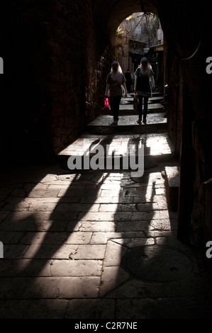 Zwei palästinensische Frauen gehen durch einen Bogen in einer alten Stadtstraße Jerusalem mit starken Schatten. Stockfoto