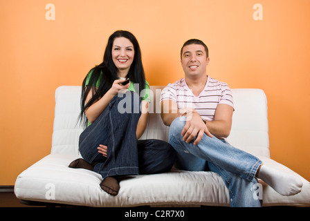 Glückliches junges Paar auf Sofa vor dem Fernseher, wechseln Sie die Kanäle und Spaß haben Stockfoto