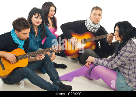 Freunde genießen die Zeit zusammen, Jungs spielen akustische Gitarren und die Mädchen hören sie und alle am Boden Stockfoto