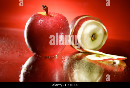 Zwei rote Äpfel auf dem Spiegel mit Tröpfchen mit rotem Hintergrund. Ein Apfel eine teilweise geschält. Stockfoto