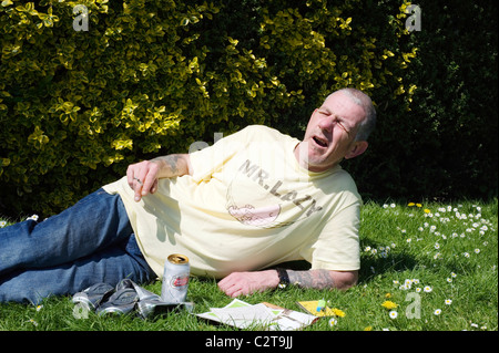 arbeitsloser Mann im öffentlichen Park genießen Sie die Sonne mit Vorteile Broschüren Bier und Zigaretten Stockfoto