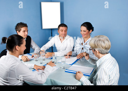 Fünf Geschäftsleute um einen Tisch zu treffen, gemeinsam lachen und uns auf Papieren von einer Geschäftsfrau, leere Tabelle Stockfoto