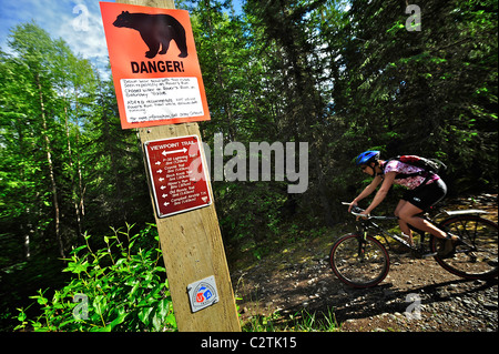 Frau reitet durch ein Bär Warnzeichen auf dem Aussichtspunkt Trail in der Nähe von Campbell Airstrip im Bicentennial Park, Anchorage, Alaska Stockfoto