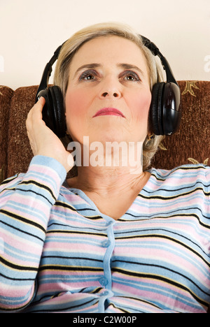 Schönheit senior Frau auf der Couch sitzen und Musik im Kopfhörer, hören sie nachschlagen und hielt ihre Hand, Kopfhörer Stockfoto