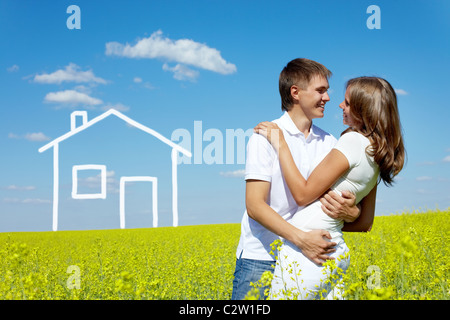 Bild des glücklichen Paares umfassend in Wiese mit gezeichneten Haus auf Hintergrund Stockfoto