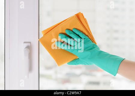 Die Hand in einem grünen Handschuh wäscht ein Fenster Stockfoto