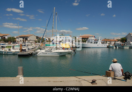 Mann Angeln an einem Kanal mit Marina von Les-Saintes-Mariés-de-la-Mer in der Camargue, Bouches-du-Rhône, Südfrankreich. Stockfoto