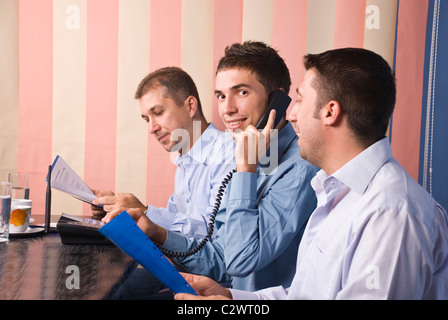Gruppe von drei Geschäftsleute in Büro, Fokus auf Mitte des Menschen, die am Telefon und lächelnd, letzte Mann liest einige Formalitäten spricht Stockfoto