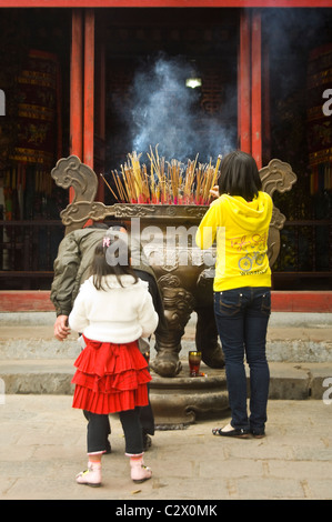 Vertikale Nahaufnahme von zwei jungen Mädchen beten und Beleuchtung Weihrauch in eine große Pfanne in Ngoc Son Tempel im Zentrum von Hanoi. Stockfoto