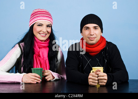 Glückliches Paar in Winterkleidung Stand am Tisch und genießen Sie zusammen eine Tasse Heißgetränk und lächelnd Stockfoto