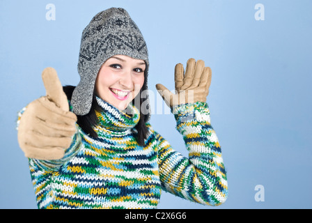 Happy Winter Mädchen in Hut und Handschuhe Daumen aufgeben auf blauem Hintergrund, Textfreiraum für SMS im rechten Teil des Bildes Stockfoto