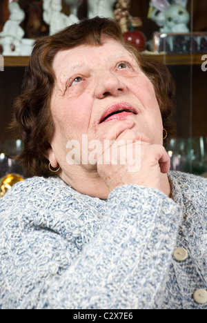 Alte Frau denken, hielt ihre Hand zum Kinn und nachschlagen Stockfoto