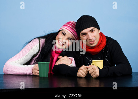 Liebevolle paar gekleidet in warme Kleidung am Tisch sitzen und genießen gemeinsam ein Heißgetränk auf blauem Hintergrund Stockfoto