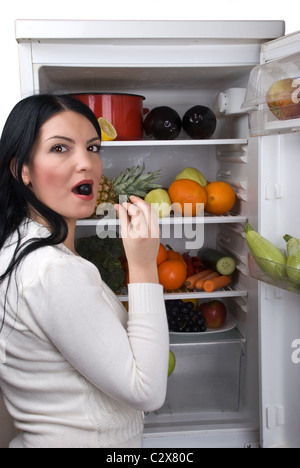 Frau mit offenen voller Kühlschrank mit Obst und Gemüse eine Beere-Traube in den Mund nehmen Stockfoto