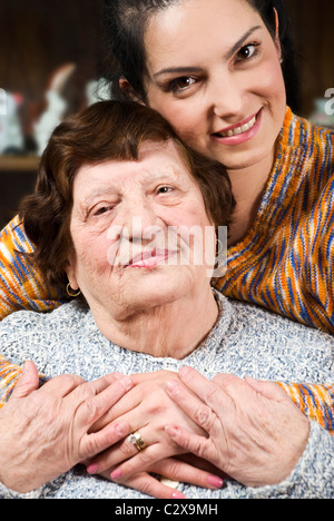 Porträt eines glücklichen Oma und Enkelin sitzt in einer Umarmung mit ihren Händen zusammen im Wohnzimmer Stockfoto
